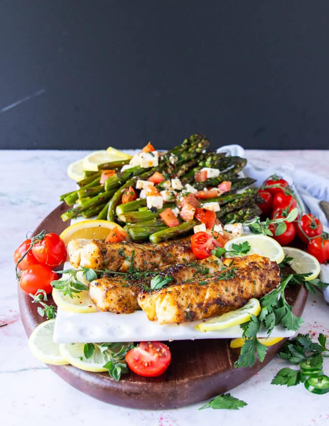 A full plate of air fryer cod surrounded by lemon wedges and herbs and baby tomatoes