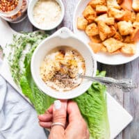 A hand holding a bowl with the salad dressing ingredients ready to be whisked and blended.