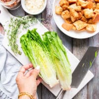A hand using a knife to cut the romaine in half