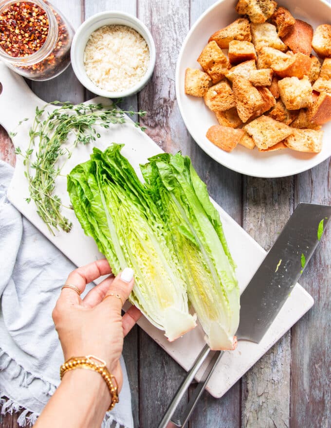 A hand using a knife to cut the romaine in half