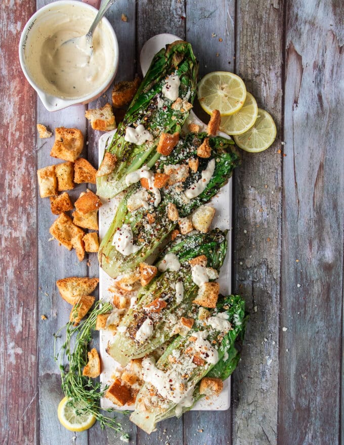 A plate of charred grilled romaine, a salad dressing on the side and crunchy toppings on the side with lemon slices