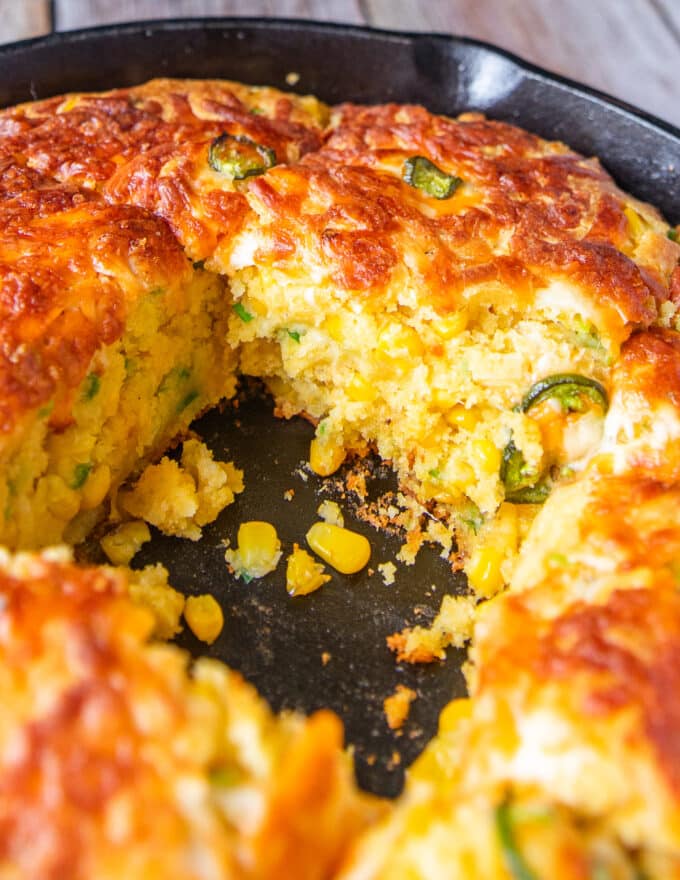 close up of a jalapeno cornbread in a skillet with a piece cut off showing the tender insides