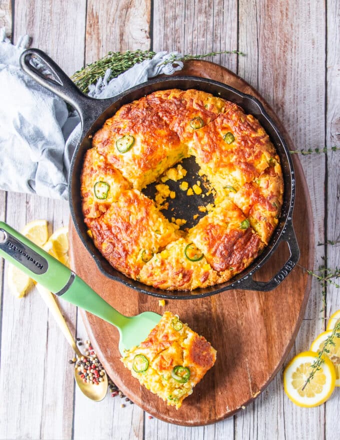 A cornbread skillet with a piece taken off on the board showing the top view of jalapeno cornbread with melted butter ontop