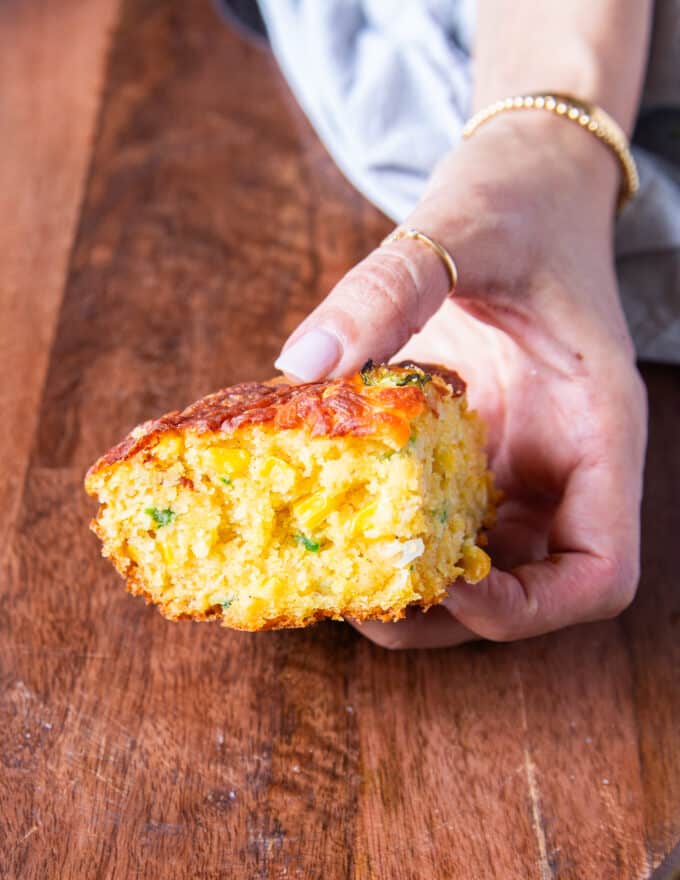 A hand holding a piece of jalapeno cheddar cornbread close up showing the texture and pieces inside
