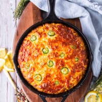Top view of a jalapeno cornbread baked in a cast iron skillet with jalapeno slices on top and cheddar cheese