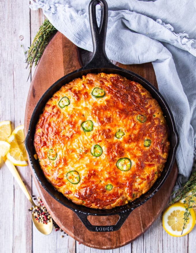 Top view of a jalapeno cornbread baked in a cast iron skillet with jalapeno slices on top and cheddar cheese