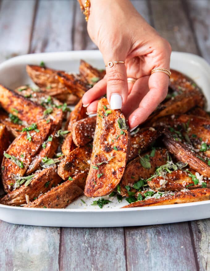 A hand holding a potato wedge close up showing how crispy the outside is and showing off the bold seasoning