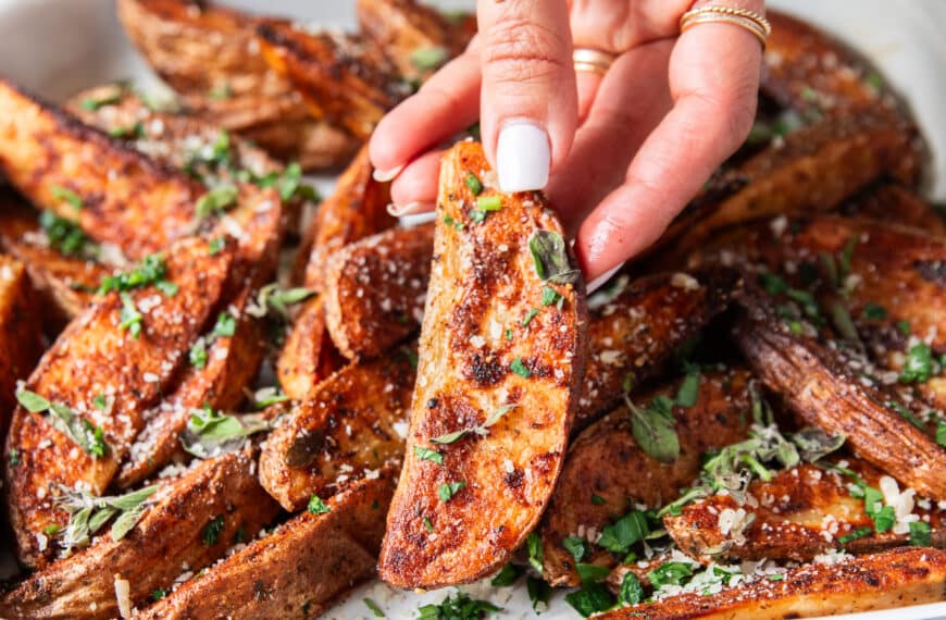 A hand holding a potato wedge close up showing how crispy the outside is and showing off the bold seasoning