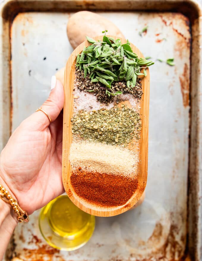 A hand holding a large plate with different seasonings for the potato wedge seasoning and some herbs