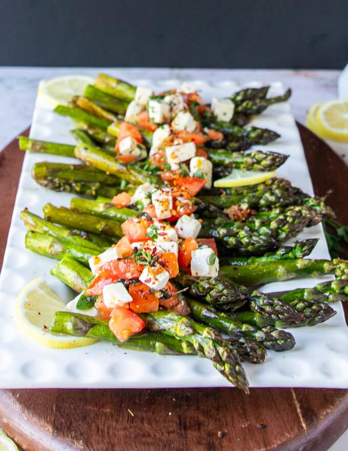 close up of a hand adding in the feta tomato and herb mix sprinkled over the baked asparagus for finishing the dish