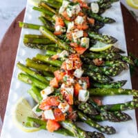 A plate with baked asparagus topped with some feta cheese and lemon slices on a plate close up showing the tender and crisp asparagus