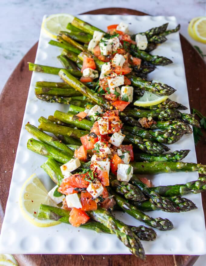 A plate with baked asparagus topped with some feta cheese and lemon slices on a plate close up showing the tender and crisp asparagus
