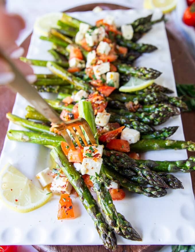 A fork holding a few roasted asparagus spears with some toppings, lemon juice and olive oil