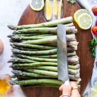 a bunch of asparagus on a wooden board and knife trimming the edges out