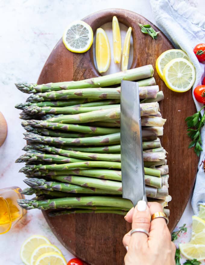 a bunch of asparagus on a wooden board and knife trimming the edges out
