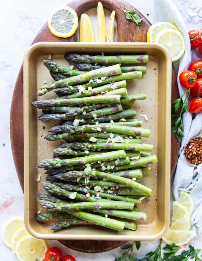 Asparagus arranged on a baking sheet in a single layer and seasoned with olive oil, garlic and seasoning