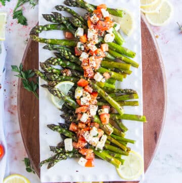 A plate with baked asparagus topped with fresh tomatoes and feta mixture for a light side dish.