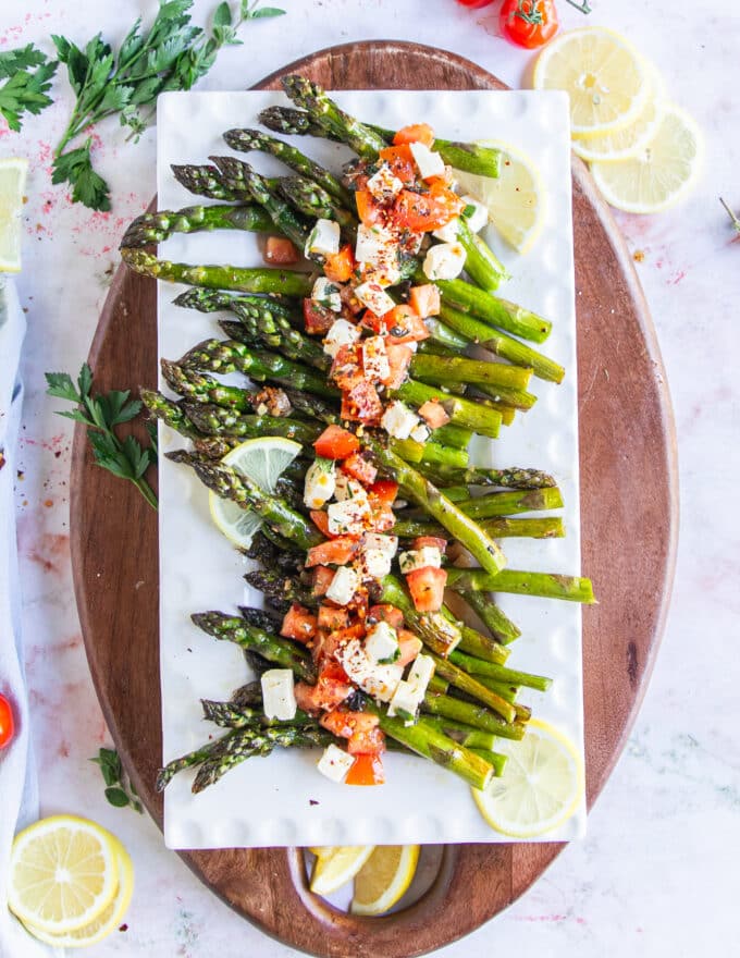 A plate with baked asparagus topped with fresh tomatoes and feta mixture for a light side dish.