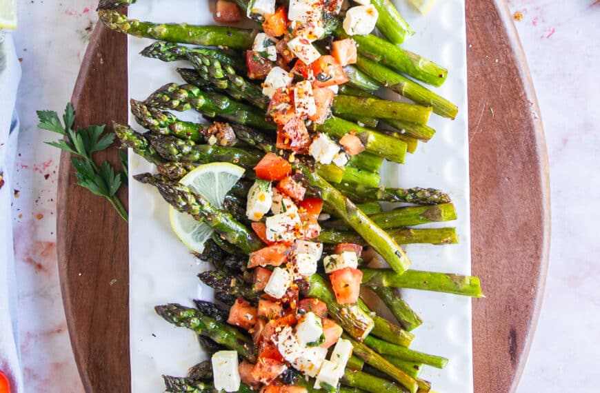 A plate with baked asparagus topped with fresh tomatoes and feta mixture for a light side dish.