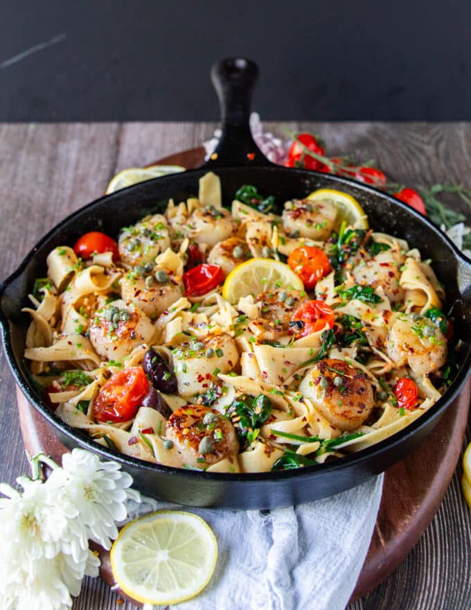 The scallop pasta ready and cooked in one pan with the golden scallops, green spinach and red tomatoes along with other ingredients showing.