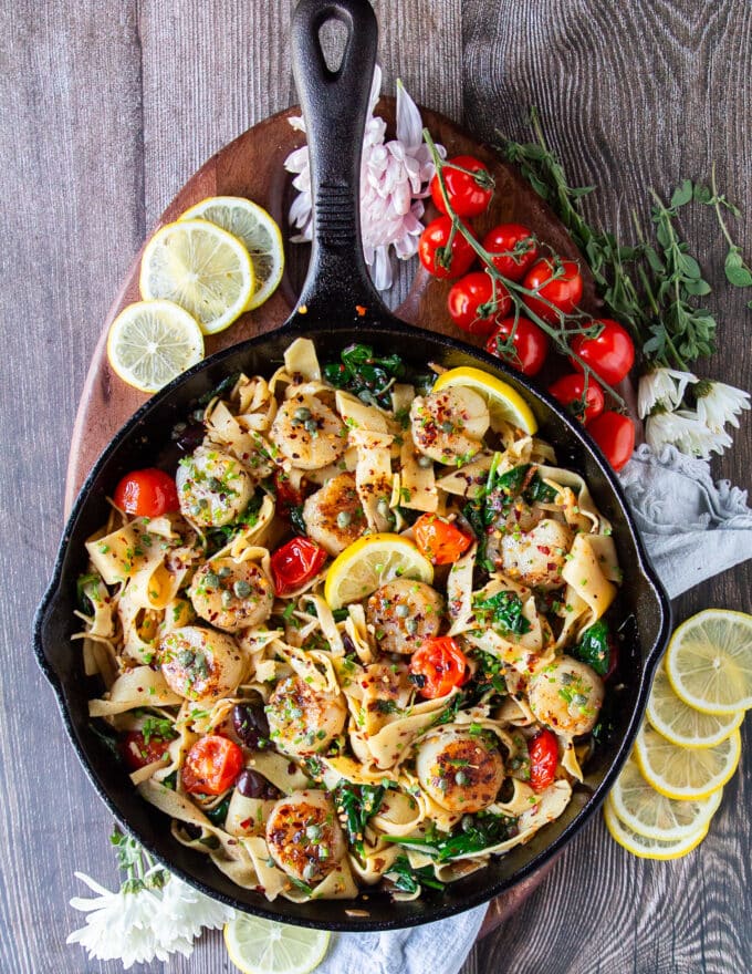 full top view of scallop pasta with lemon wedges for serving and cherry tomatoes on the vine on the side