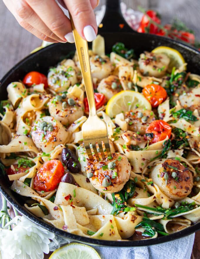 A fork biting into a tender golden scallop over the scallop pasta recipe.